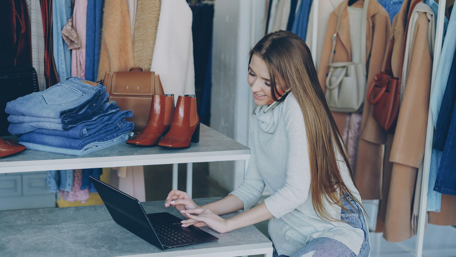 Shopbetreiberin arbeitet am Laptop zwischen Kleidern und Schuhen